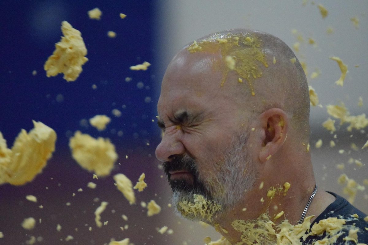 Eighth grader George Stewart throws a pie at his coach, Mr. Thombs, while Mr. Thombs purposely scoots his chair forward to ensure he isn’t hit. In the end, he was hit straight in the face as everyone screamed with cheers. 
